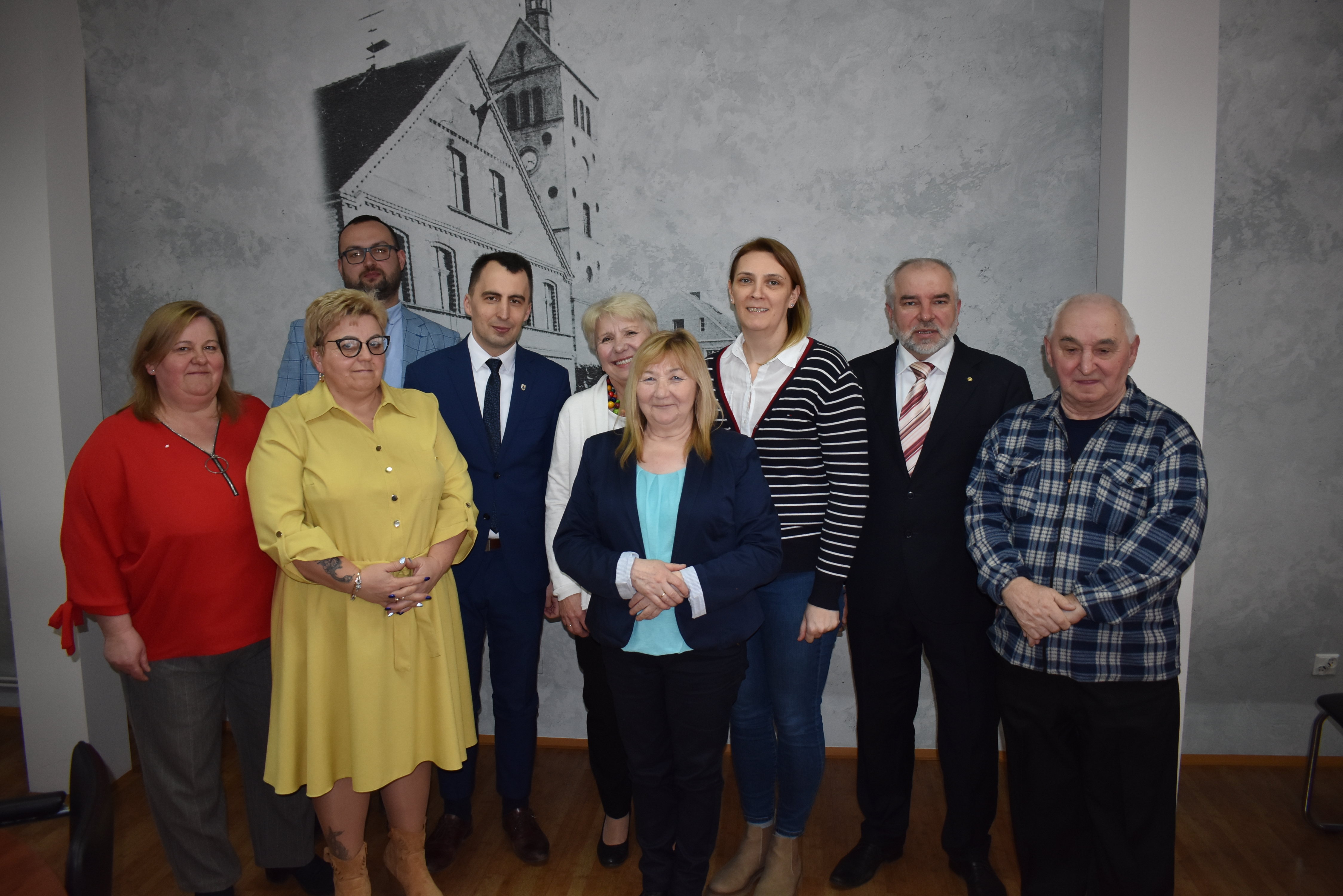 Dziewięć os&oacute;b stoi na&nbsp;tle starej fotografii