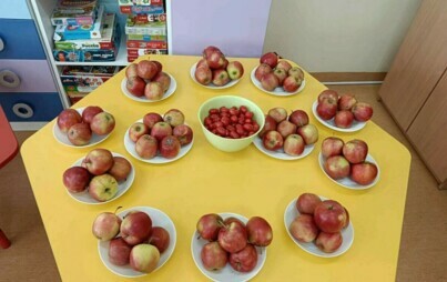 sześciokątny stół na talerzach jabłka oraz miseczka pomidorów koktajlowych