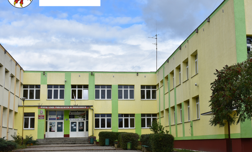 zdjęcie przodu szkoły w Dobrzanach. W lewym górnym rogu herb Gminy Dobrzany oraz logo Państwowy Fundusz Rehabilitacji Osób Niepełnosprawnych